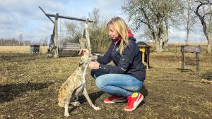 Sieviete lauku vidē glauda raibu vipetu, fonā redzama pavasarīga daba