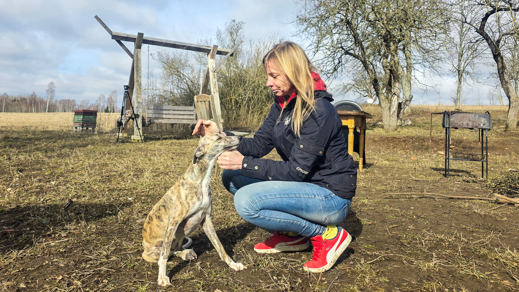 Sieviete lauku vidē glauda raibu vipetu, fonā redzama pavasarīga daba