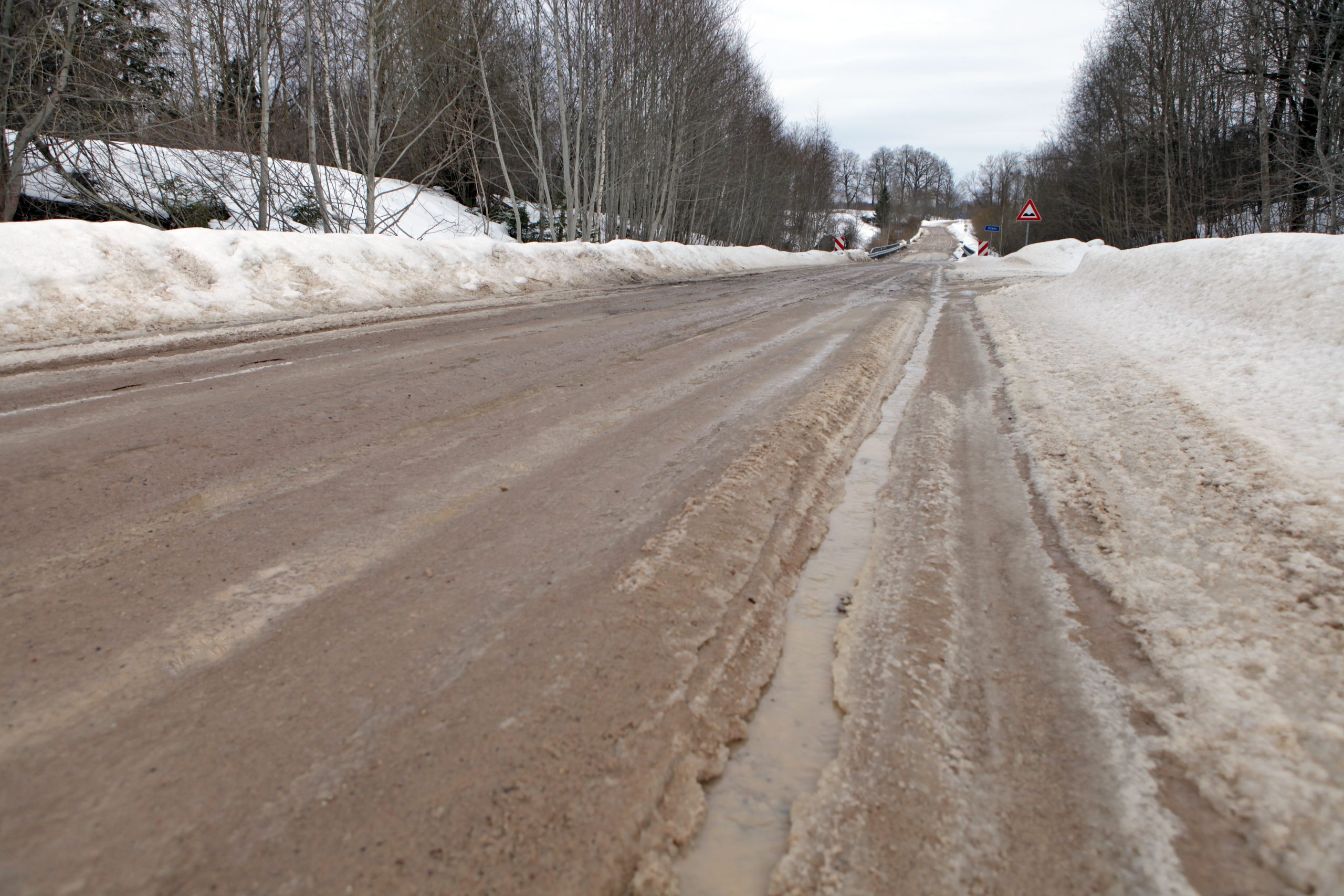 Sniegots lauku autoceļš ar apledojumu un ceļa zīmēm ziemas apstākļos.