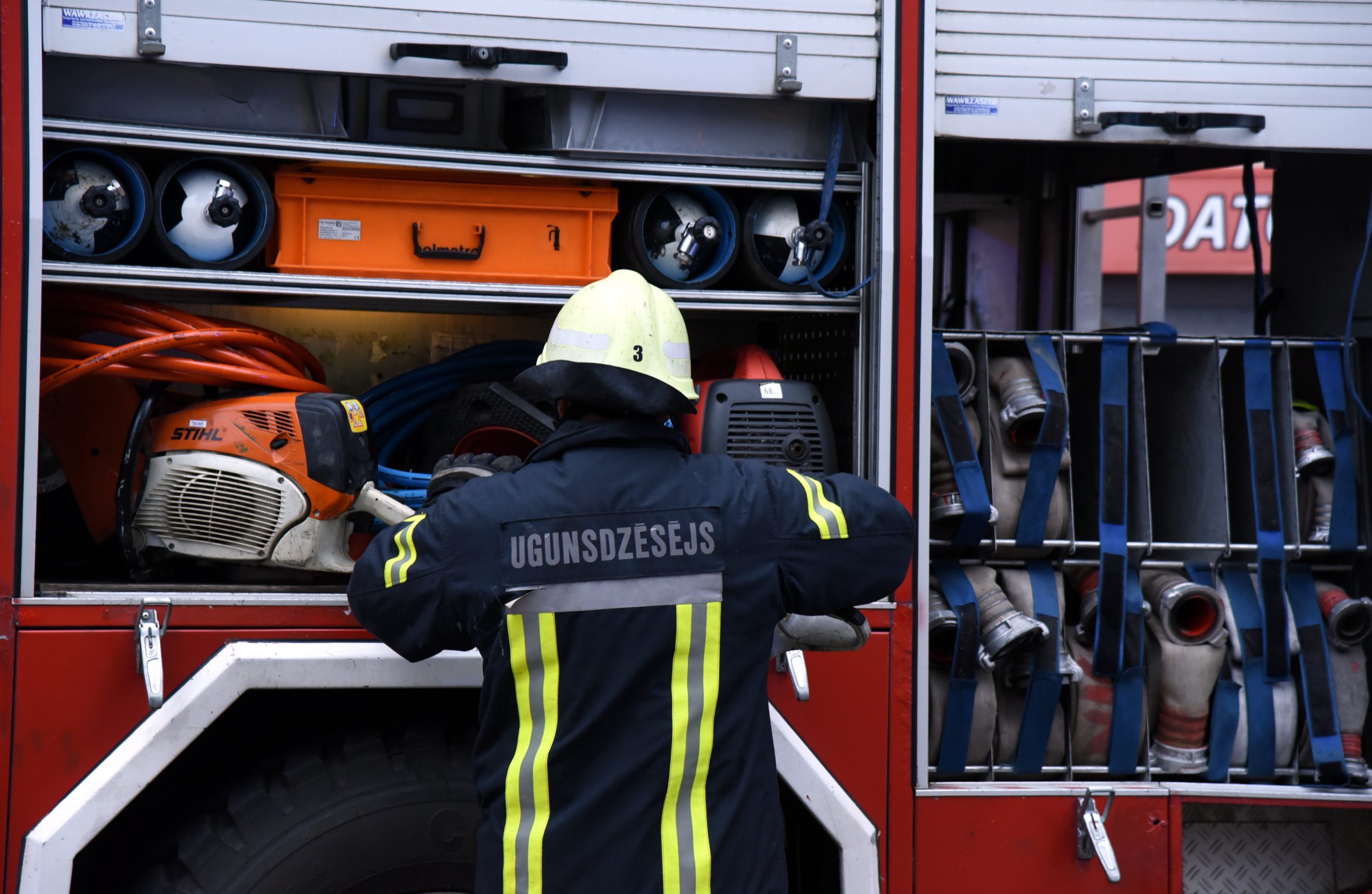 Ugunsdzēsējs pie ugunsdzēsības transportlīdzekļa ar aprīkojumu.