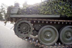Militārās bruņutehnikas kāpurķēžu tuvplāns ar maskēšanās tīklu.