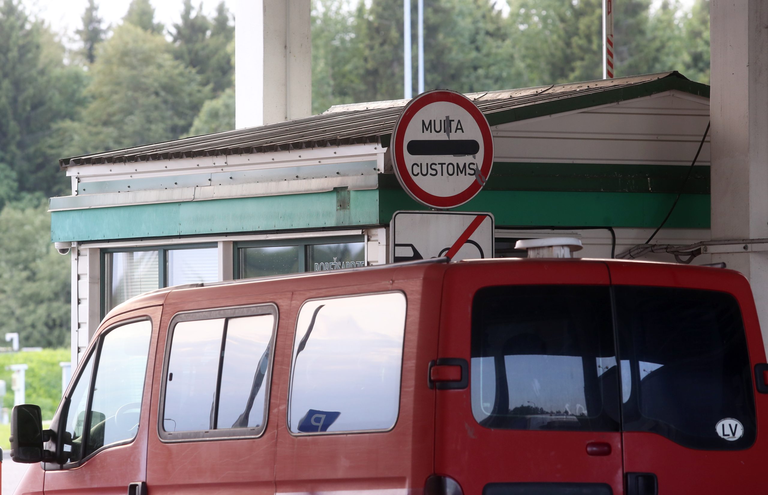 Latvijas muitas kontroles punkts ar sarkanu mikroautobusu pie robežas.