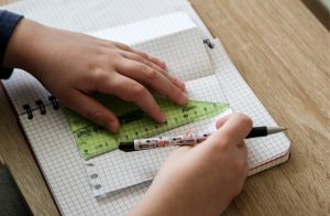 Bērna rokas, kas raksta kladē un izmanto lineālu.
