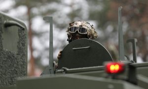 Karavīrs bruņutransportierī ar aizsargbrillēm un maskēšanās ķiveri, skatoties no transportlīdzekļa lūkas
