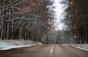 Ziemas ceļš ar sniegotiem kokiem un ātruma ierobežojuma zīmi