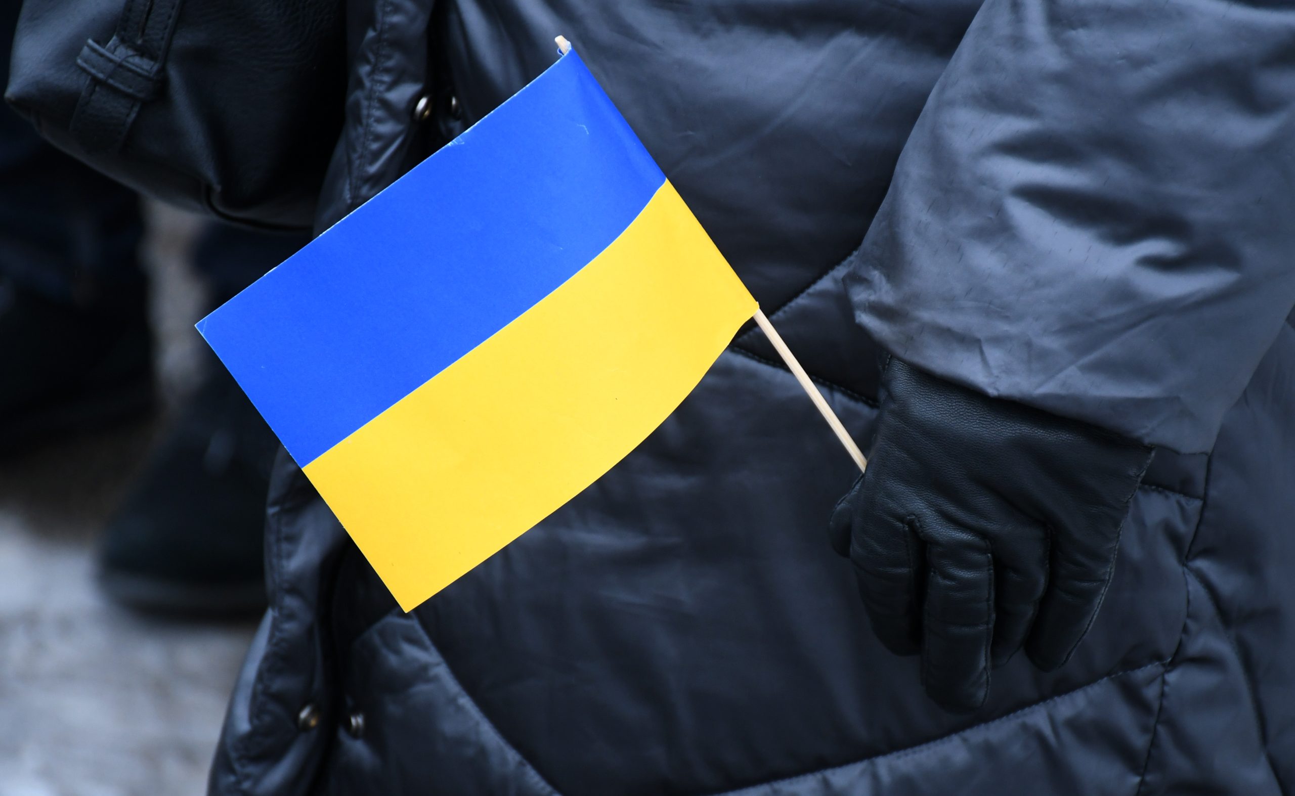 Persona melnā jakā un cimdos tur Ukrainas karodziņu.