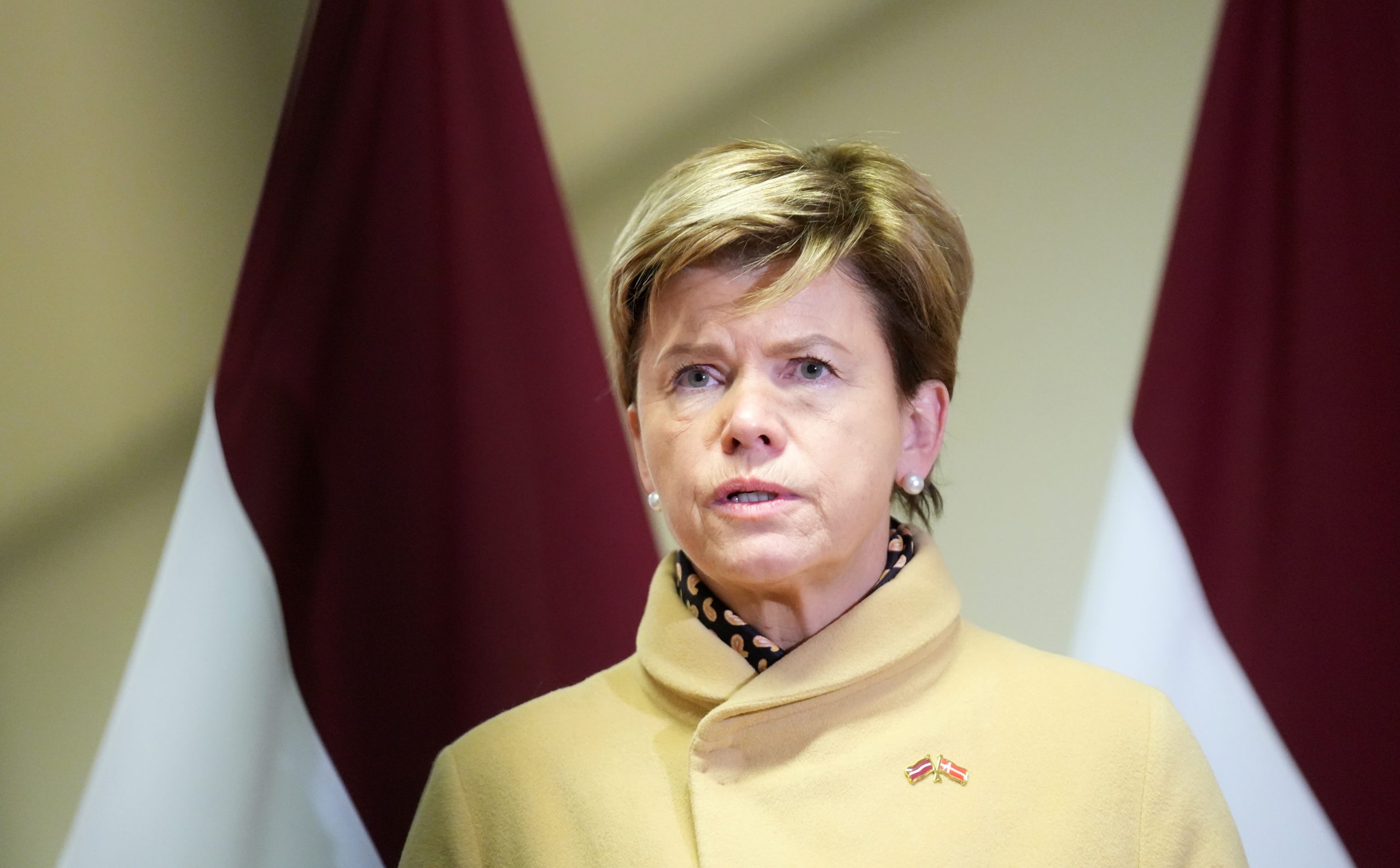 Latvijas ārlietu ministre Baiba Braže mētelī preses konferencē, fonā redzami Latvijas karogi