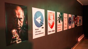 Vairāki politiska satura plakāti, kas izvietoti uz sienas vienā rindā, atspoguļojot kritisku skatījumu uz dezinformāciju un autoritārisma problēmām