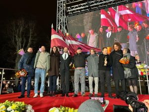 Filmas "Straume" komanda tiek sagaidīta Rīgā pēc "Oskara" iegūšanas, stāvot uz sarkanā paklāja ar Latvijas karogiem fonā.