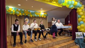 Bērni un jaunieši uz skatuves festivālā “Saules stariņi”, izpildot muzikālu priekšnesumu ar dziedāšanu un instrumentiem.