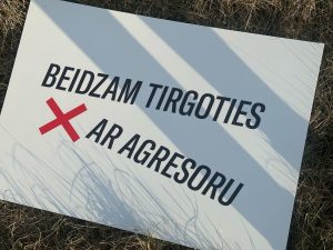 Protesta plakāts ar uzrakstu "Beidzam tirgoties ar agresoru" uz zāles
