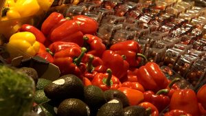 Alt text: Svaigi sarkanie un dzeltenie pipari, avokado un ķirštomāti veikalā.