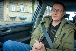 Vīrietis ar brillēm automašīnā, piesprādzējies ar drošības jostu