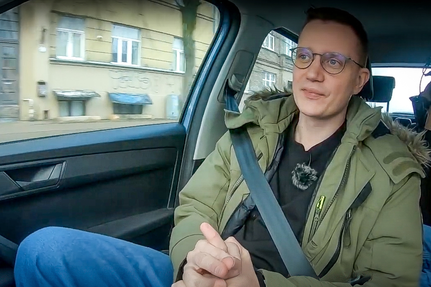 Vīrietis ar brillēm automašīnā, piesprādzējies ar drošības jostu