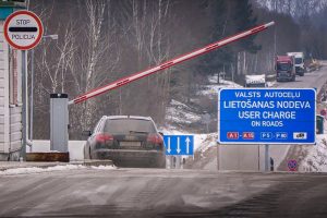 Auto pie paceltas barjeras, blakus ceļa zīme Stop policija un valsts autoceļu lietošanas nodevas norāde