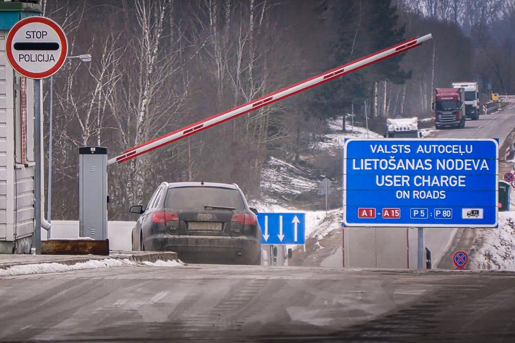 Auto pie paceltas barjeras, blakus ceļa zīme Stop policija un valsts autoceļu lietošanas nodevas norāde