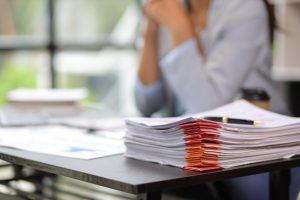 Dokumentu kaudze uz rakstāmgalda ar neskaidru sievietes siluetu fonā