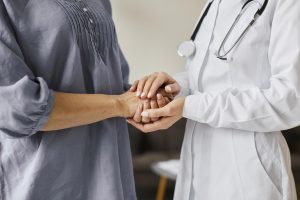 Ārste tur pacienta rokas, simbolizējot uzticēšanos un atbalstu ārstēšanās procesā