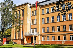 Cēsu Valsts ģimnāzijas ēka ar Latvijas karogu pie ieejas.