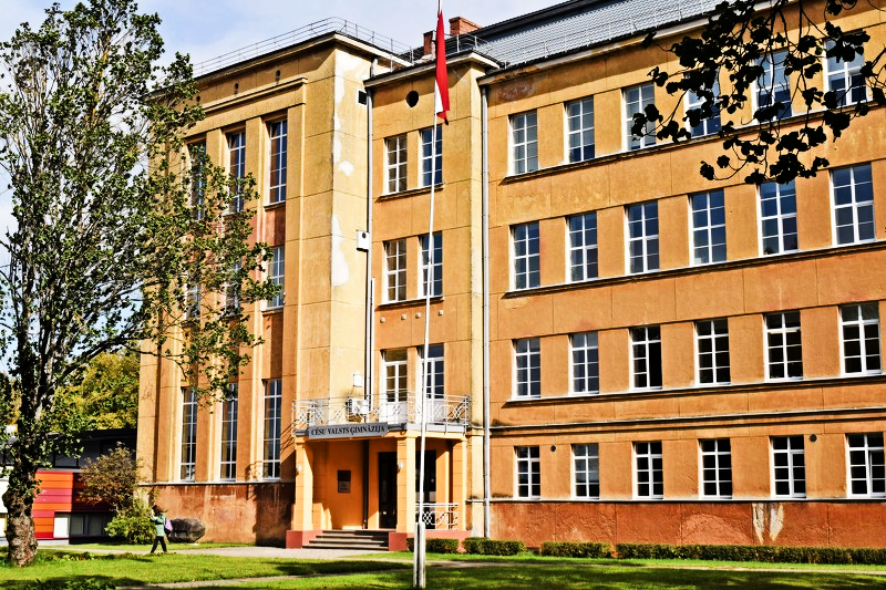 Cēsu Valsts ģimnāzijas ēka ar Latvijas karogu pie ieejas.