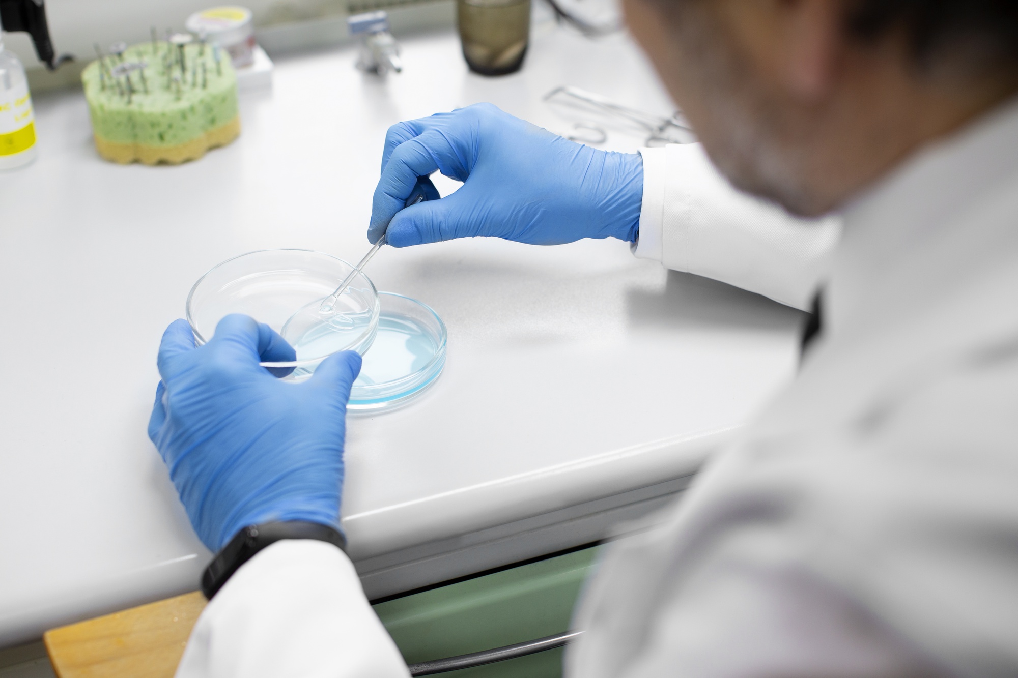 Zinātnieks laboratorijā veic mikrobioloģisku analīzi, izmantojot Petri trauku un pipeti.
