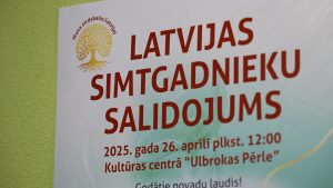 Latvijas Simtgadnieku salidojuma plakāts ar pasākuma norises datumu un vietu