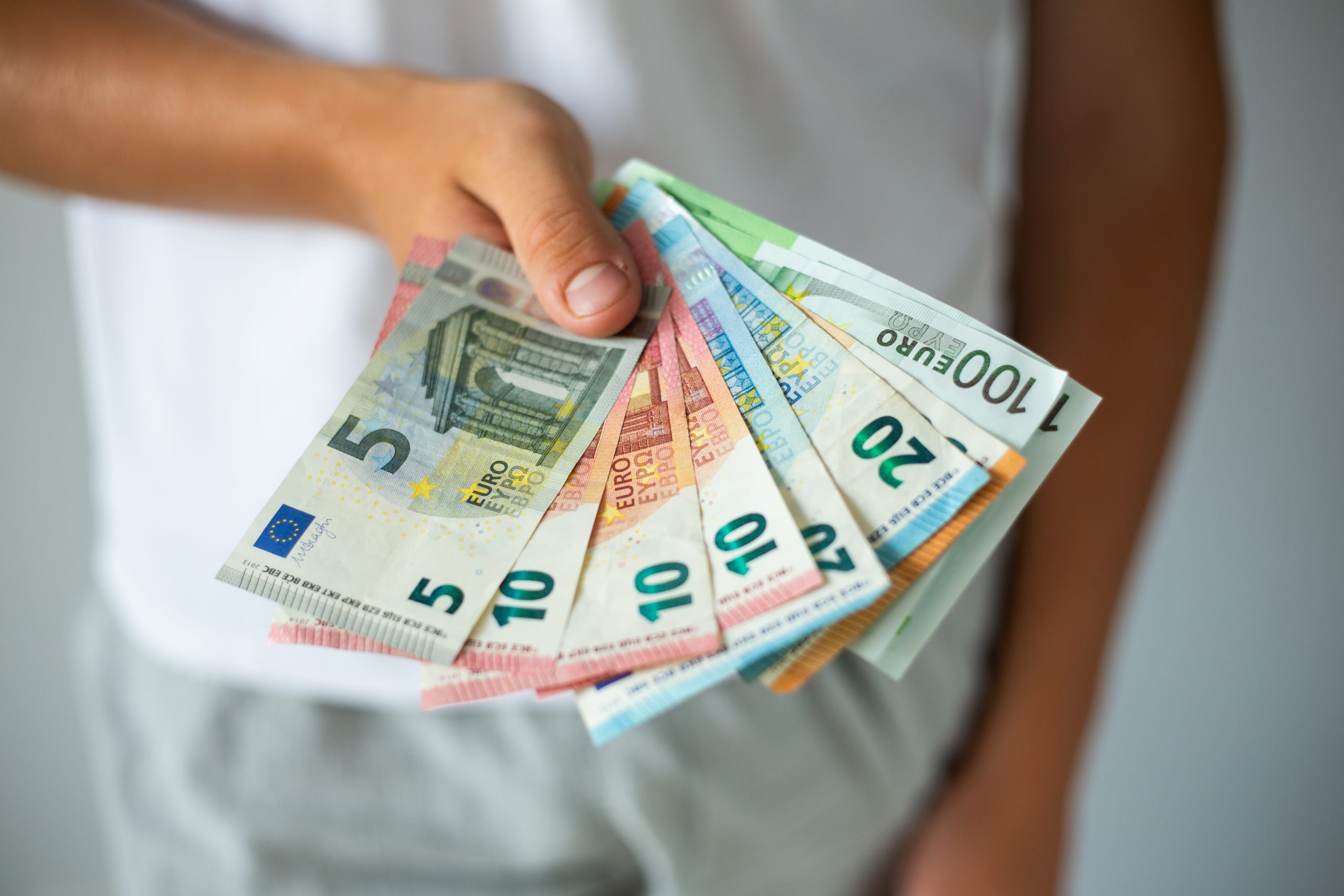 Rokas, kas tur eiro banknotes dažādos nominālos.