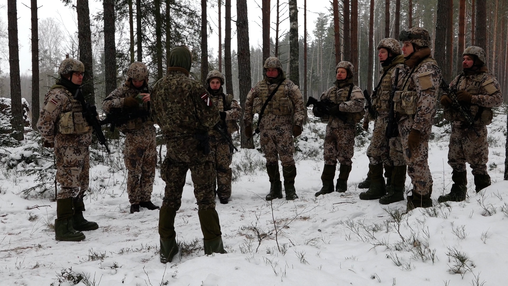 Latvijas karavīri ziemas apstākļos apmācību laikā mežā.