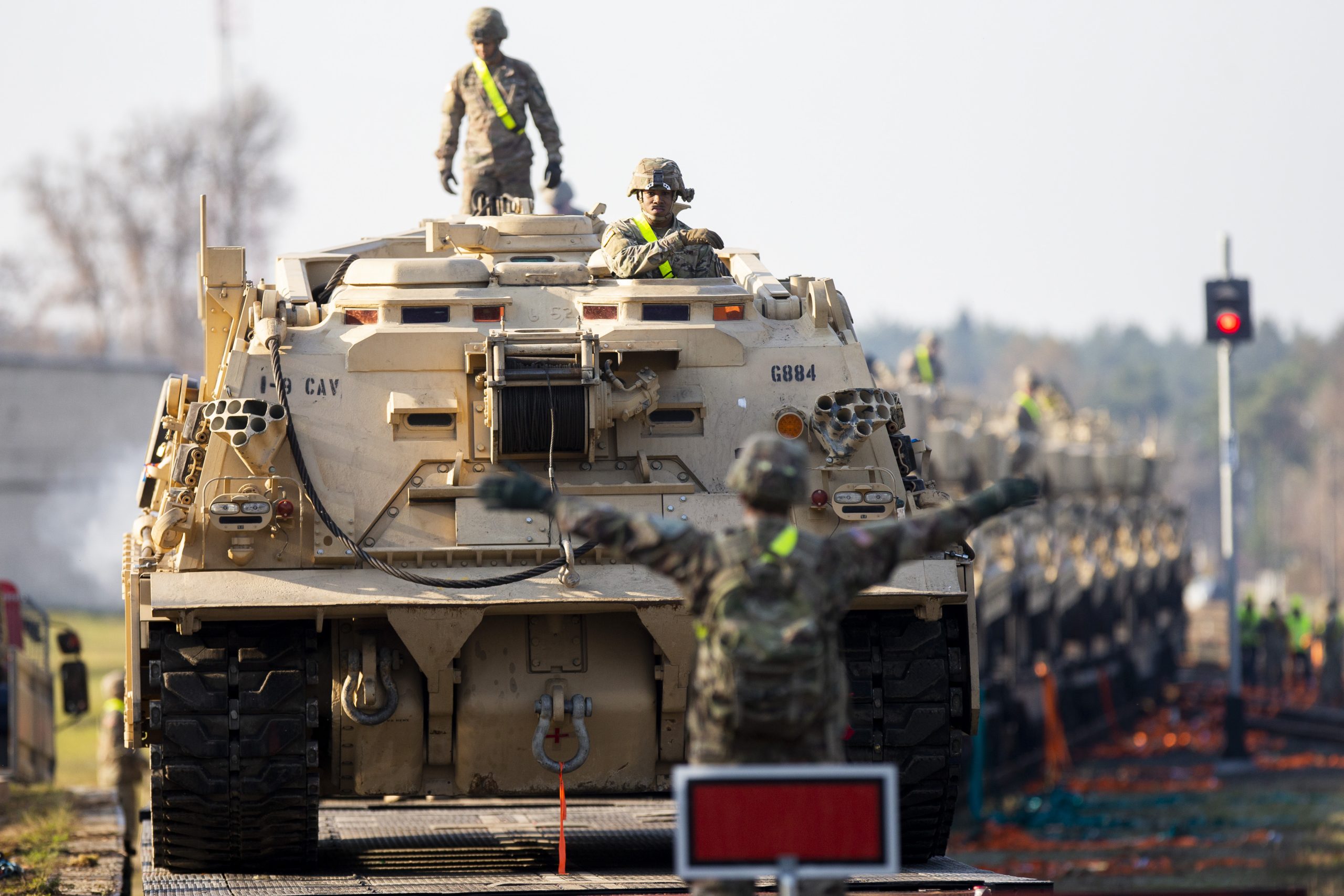 Bruņutransportieri uz dzelzceļa platformām, ko vada karavīri, gatavojoties militārai pārvietošanai