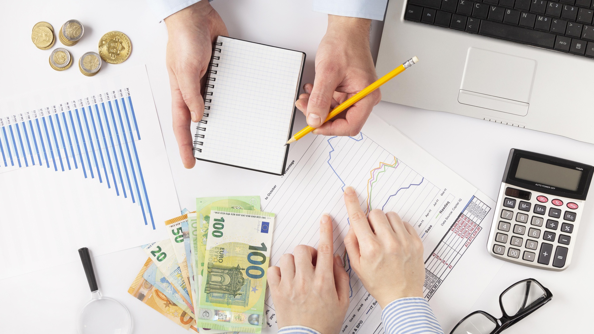 Rokas ar naudu, kalkulatoru un grafikiem, kas simbolizē finanšu plānošanu