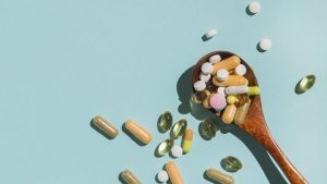 Karote ar dažādiem vitamīniem un uztura bagātinātājiem uz zilganzaļa fona