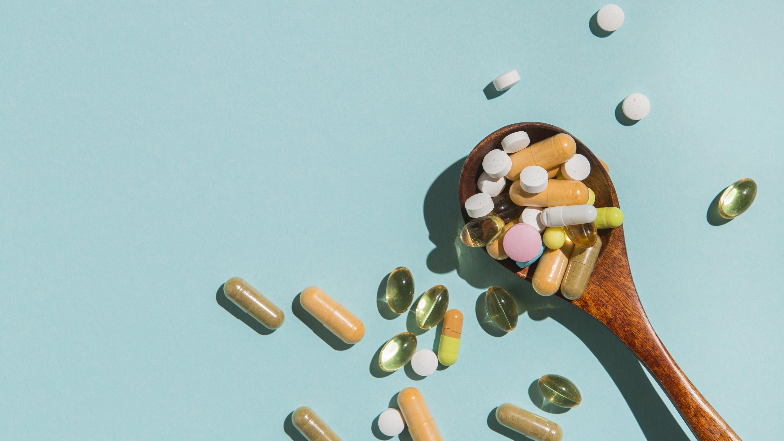 Karote ar dažādiem vitamīniem un uztura bagātinātājiem uz zilganzaļa fona