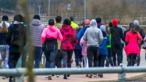 Cilvēku grupa, kas skrien kopīgā treniņā uz ielas, ģērbušies košās sporta drēbēs