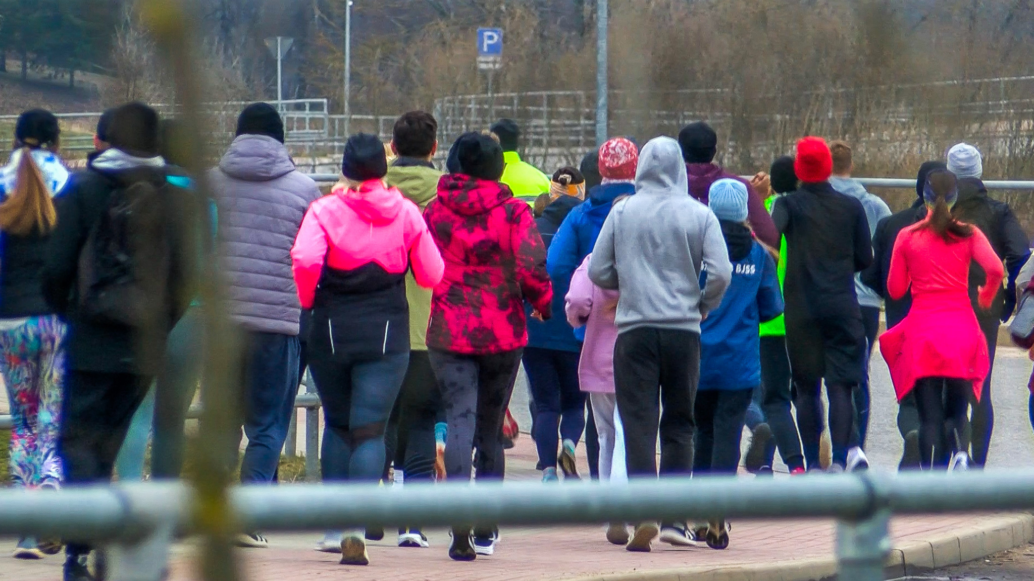 Cilvēku grupa, kas skrien kopīgā treniņā uz ielas, ģērbušies košās sporta drēbēs