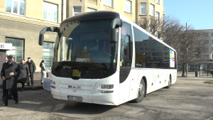 Balts MAN autobuss ar uzrakstu "Stand with Ukraine" uz priekšējā stikla, novietots pilsētas laukumā, apkārt cilvēki