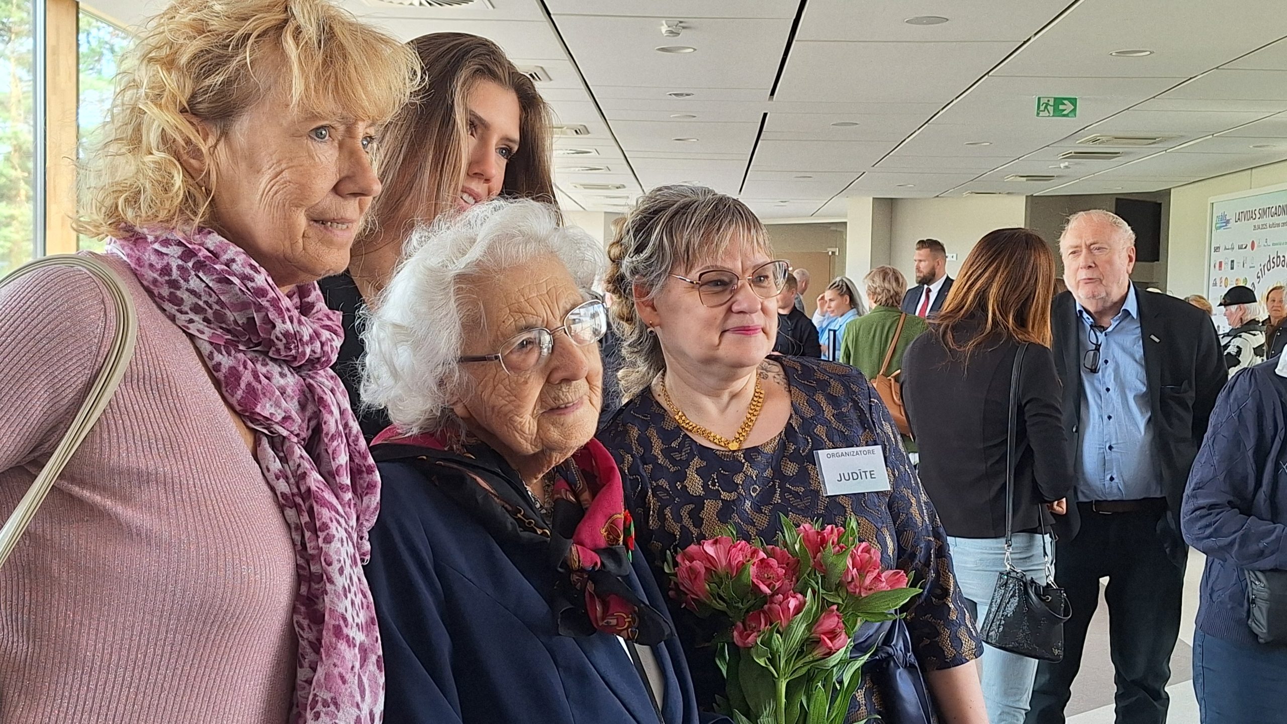 Cilvēki svinīgā pasākumā pozē kopīgai fotogrāfijai