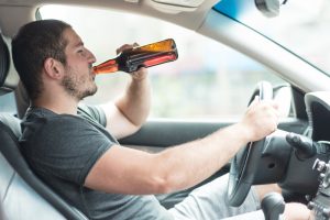 Vīrietis dzer alu pie automašīnas stūres