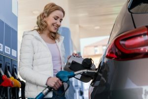 Sieviete smaidot uzpilda automašīnu ar degvielu pie degvielas uzpildes stacijas.