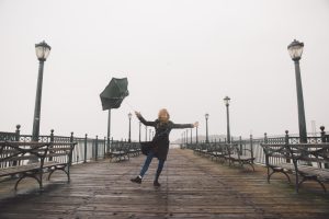 Sieviete ar izpūstu lietussargu skrien pa tukšu promenādi vējainā dienā