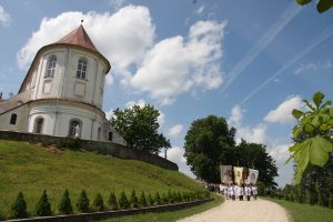 Reliģiskā procesija ar karogiem pie vēsturiskas baznīcas zem zilām debesīm