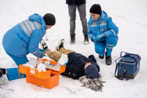Neatliekamās medicīniskās palīdzības darbinieki palīdz cilvēkam, kurš guļ sniegā