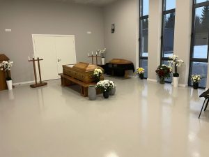 Atvadu ceremonijas zāle ar ziediem un zārku.