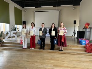 Apbalvošanas ceremonija ar laureātiem uz skatuves, rokās turot diplomus