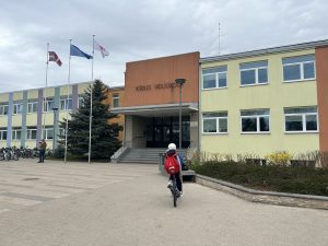 Skolēns ar sarkanu mugursomu tuvojas Ikšķiles vidusskolas ēkai ar velosipēdu