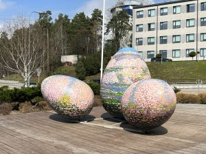 Trīs krāsainas Lieldienu olas uz koka platformas pie biroju ēkas
