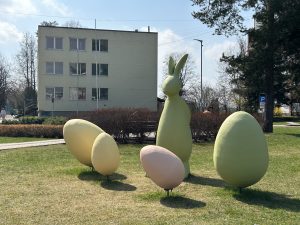 Zaļš Lieldienu zaķis ar krāsotām olām uz zāliena pie ēkas