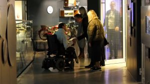 Cilvēki sarunājas ar personu ratiņkrēslā Motormuzeja telpās