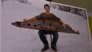 Vīrietis tur dižkokli ziemas ainavā, sēžot uz krēsla