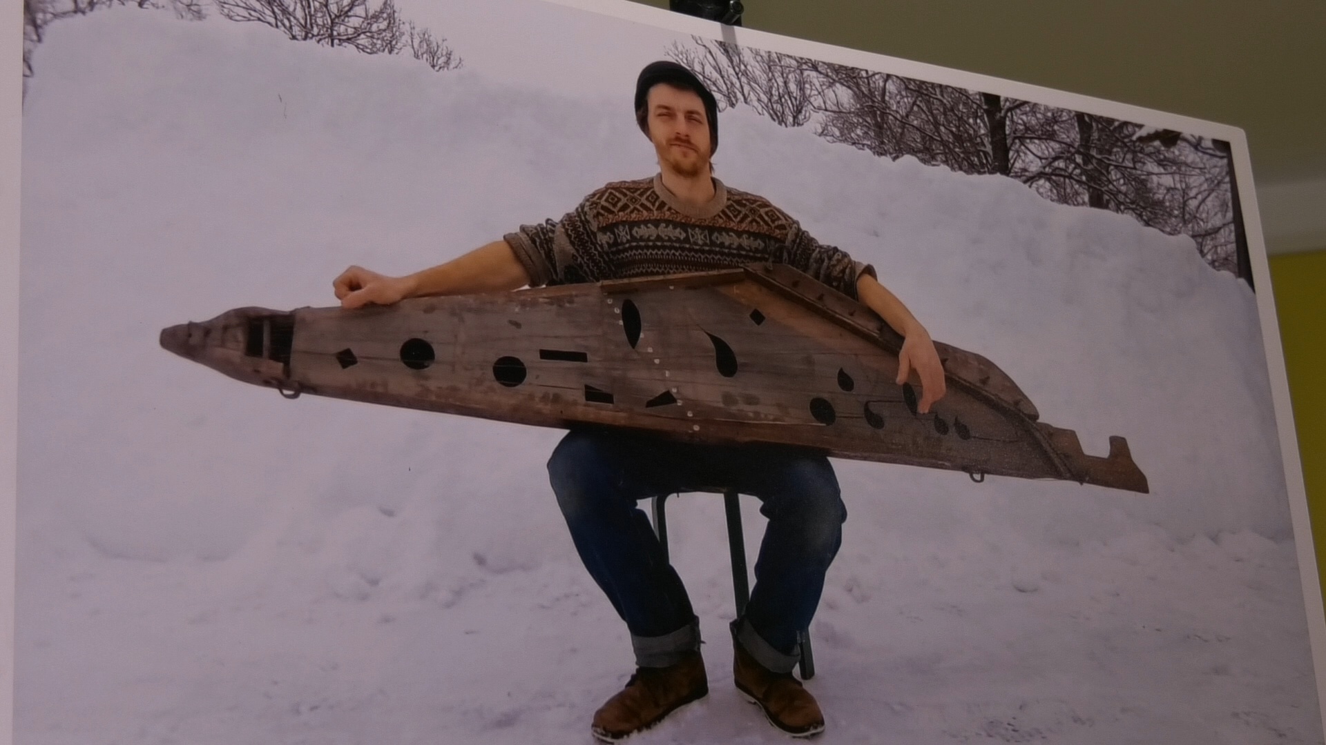 Vīrietis tur dižkokli ziemas ainavā, sēžot uz krēsla