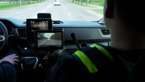 Policijas darbinieks automašīnā vēro satiksmi ar monitoringa ierīci